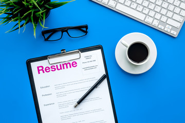 Empoyment concept. Resume on blue work desk with coffee, glasses, keyboard top view