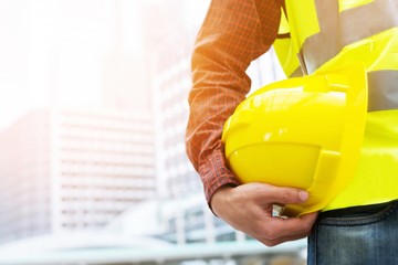 Close up front view of engineering male construction worker holding safety yellow helmet and wear...