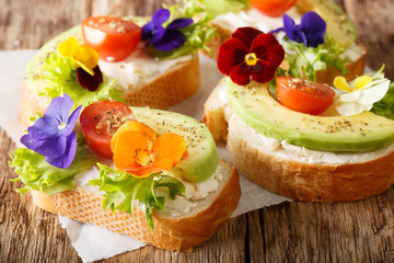 Beautiful sandwiches with avocado, tomatoes, edible flowers of viola and cream cheese close-up on...