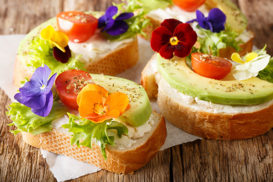 Beautiful sandwiches with avocado, tomatoes, edible flowers of viola and cream cheese close-up on the table. horizontal
