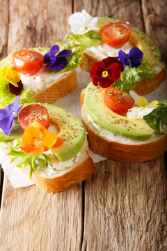 Vegetarian open sandwiches with avocado, tomatoes, edible flowers and cream cheese close-up. vertical