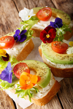 Healthy food: toasts with avocado, tomatoes, edible flowers and cream cheese close-up. vertical