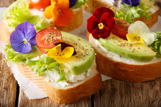 Festive toasts with avocado, tomatoes, edible flowers and cream cheese close-up. horizontal