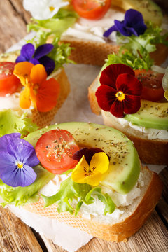 Tasty sandwiches with avocado, tomatoes, edible flowers and cream cheese close-up on the table. vertical