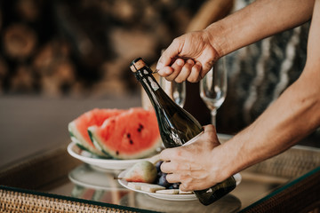 Hands open bottle of champagne. Back watermelon and fruit