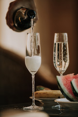Hand pours champagne into tall glasses