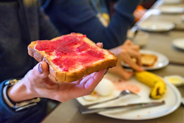 Hand holds a piece of bread with red jam