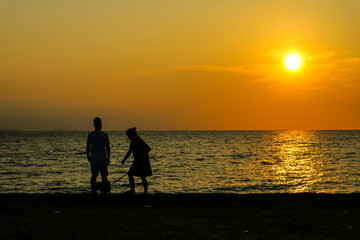 Fototapeta premium silhouette two people play with dog on beach sunset