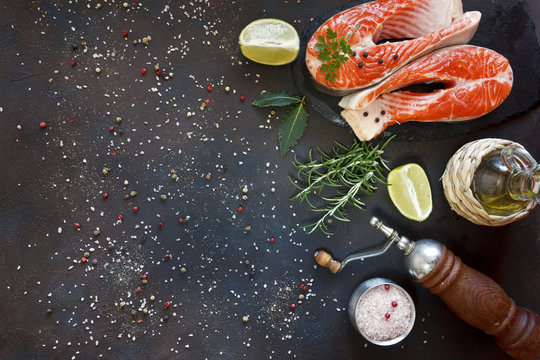 Close-up photo of fresh salmon fish with sea salt and lime slices on black table background