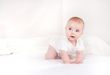 Portrait of sweet newborn infant crawlng on white bed serious looking away