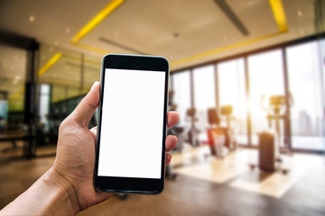 A man hand holding smart phone device in the fitness room view background in morning light
