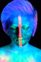 Model young beautiful girl portrait in studio with creative makeup, in neon ultraviolet lamp. Glows in the dark. Hair coloring with neon paints. Body art is blue, green, orange.