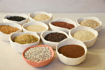 A variety of organic ancient grains in rustic handmade clay bowls on a canvas surface.