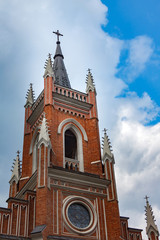 Obraz premium The building of the Catholic church with crosses and the spire on the building on a background of white clouds and a blue sky.