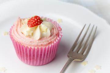 Pink strawberry cupcake on white plate with star sprinkles