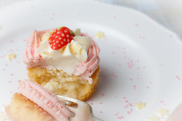 Pink strawberry cupcake on white plate with star sprinkles being eaten