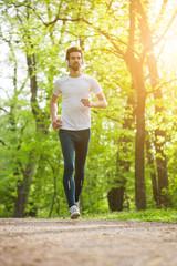 Young man is jogging in park. He is listening music on headphones.