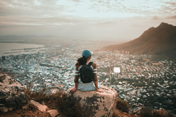 Young woman sitting on top of mountain overlooking city - Powered by Adobe