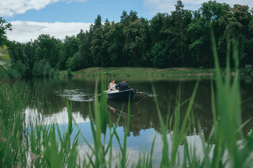 Fototapeta na wymiar beautiful young wedding couple, blonde bride with flower and her groom just married on small boat at pond
