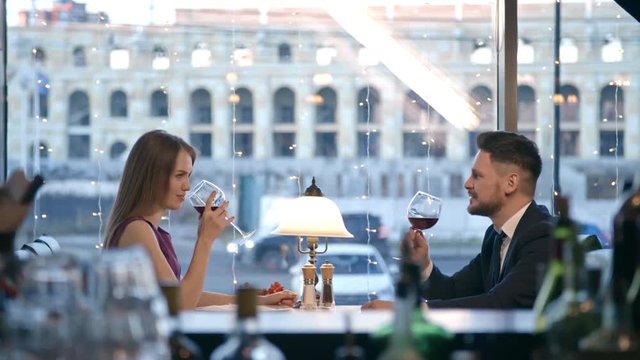 Side view of happy man and woman clinking glasses and drinking red wine on dinner date in restaurant