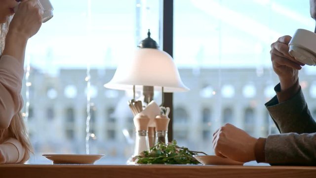 Side view of young man and woman sitting at table in cafe and drinking coffee on lunch date