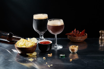 Ale and stout beer in glasses with snacks and sauce on metallic and black background