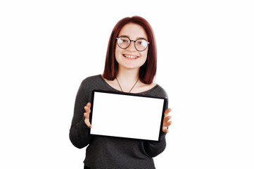 Fototapeta premium Smiling beautiful young red hair woman showing blank no-name tablet pc monitor, over white background, with copyspace area for slogan or text message