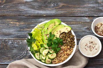 Green Buddha Bowl with lentils, quinoa, avocado, cucumber, fresh lettuce, herbs and seeds with tahini sauce. Delicious healthy balanced eating. On a wooden background, top view, free space