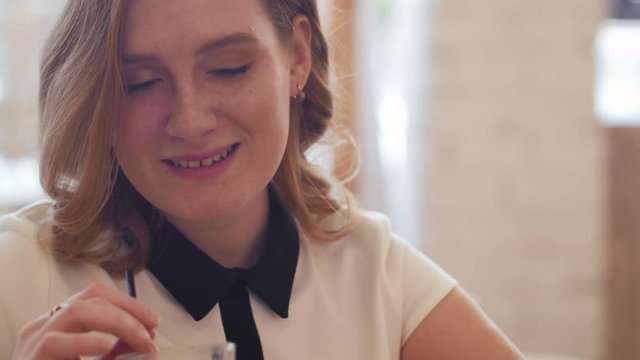 Young woman drinking coffee and speaking with frien in cafe.
