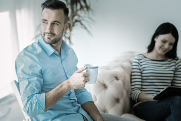 Obraz premium Coffee break. Attractive meditative reflective man looking aside while holding cup and enjoying coffee