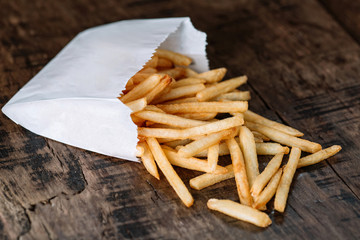 French fries potatoes in a paper bag on wood background