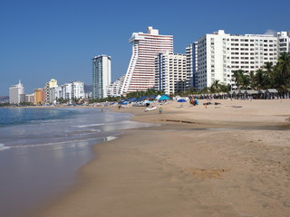 Fototapeta na wymiar Panorama of white hotel buildings on beauty sandy beach at bay of Pacific Ocean at ACAPULCO city in Mexico with tourists