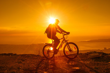 Naklejka na ściany i meble Silhouette of cyclist riding on a bike in mountain at sunset