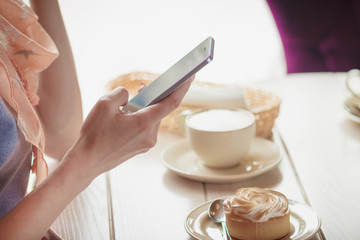 Woman in the cafe with a cup of cappuccino and a piece of dessert on the plate