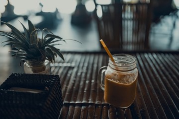 Jar with ice fruit shake and straw inside standing on the bamboo table. 