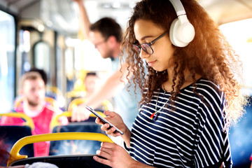 Young cheerful cute curly girl enjoying music while riding in the bus.