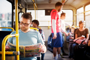 Young man is focused on reading his newspapers while taking a bus ride.