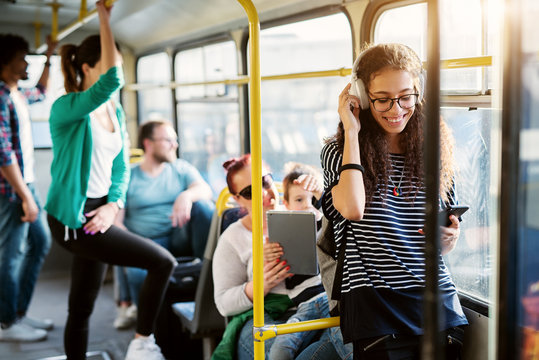 Diverse group of people is traveling by bus with the young adorable woman in the first plan of the picture who is smiling and listening to her music.