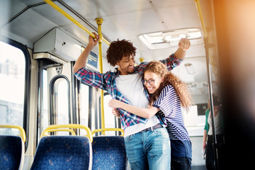 Young gorgeous playful girl is hugging her cheerful and surprised boyfriend in a bus.
