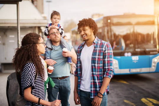 Multicultural Group Of People Standing At The Bus Stop Waiting For The Bus And Having A Conversation.