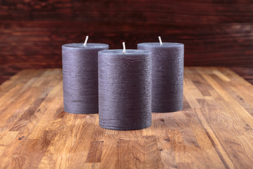 three decorative new candles are standing on an oak surface on a dark background