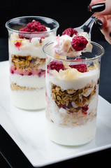granola with berries and yogurt in a glass on a white plate and a black background