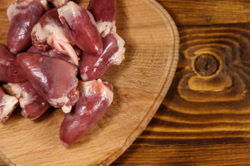 Raw chicken hearts on cutting board on wooden table