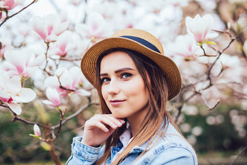 Happy beautiful young woman in spring blossom park with magnolia trees.