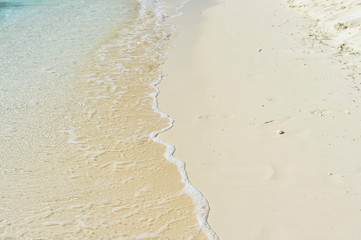 Sea wave with foam runs to the sandy shore and washed away footp