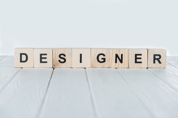 close up view of designer word made of wooden cubes on white wooden tabletop