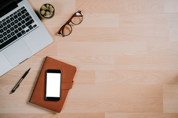 Modern office desk table with laptop,blank screen smart phone,notebook and eyeglasses.Top view with copy space.Working desk table concept.