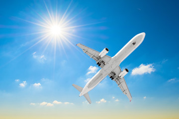 White airplane flies in a blue sky with a bright sun.