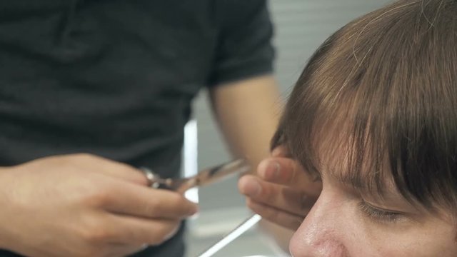 Hairdresser cuts a forelock to client in a salon. Man sitting in hairdressers armchair while shearing with scissors in barbershop.