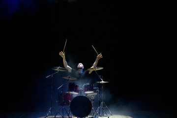Obraz premium Drummer in a cap and headphones plays drums at a concert under white light in a smoke